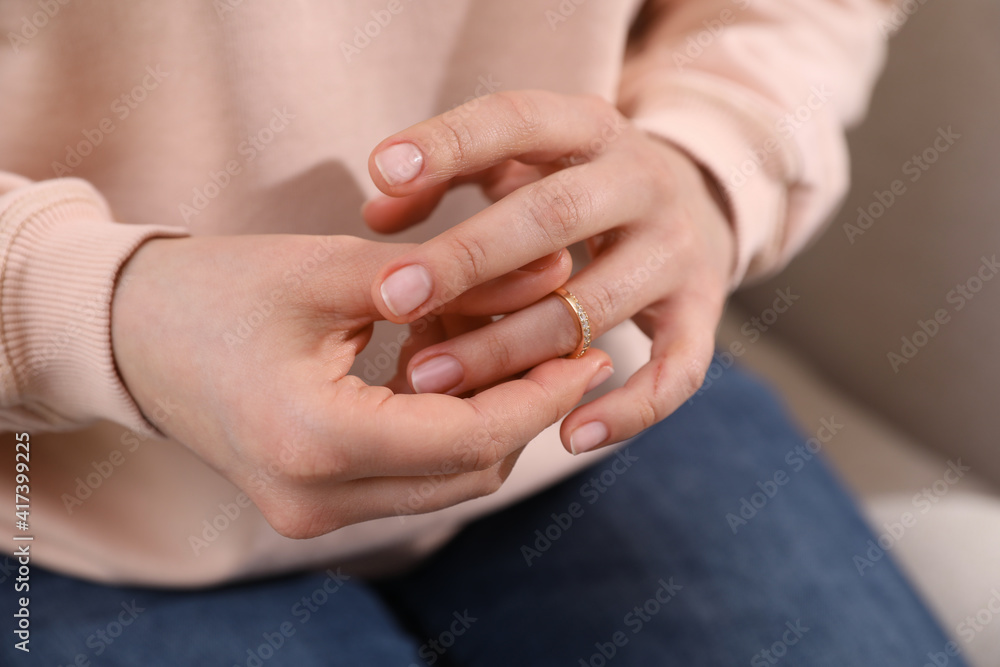 Woman taking off wedding ring on sofa, closeup. Divorce concept