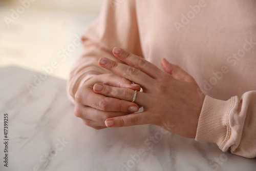 Woman taking off wedding ring at table indoors, closeup. Divorce concept