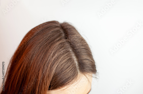 A woman's head with a parting of gray hair that has grown roots due to quarantine. Brown hair on a woman's head close-up.