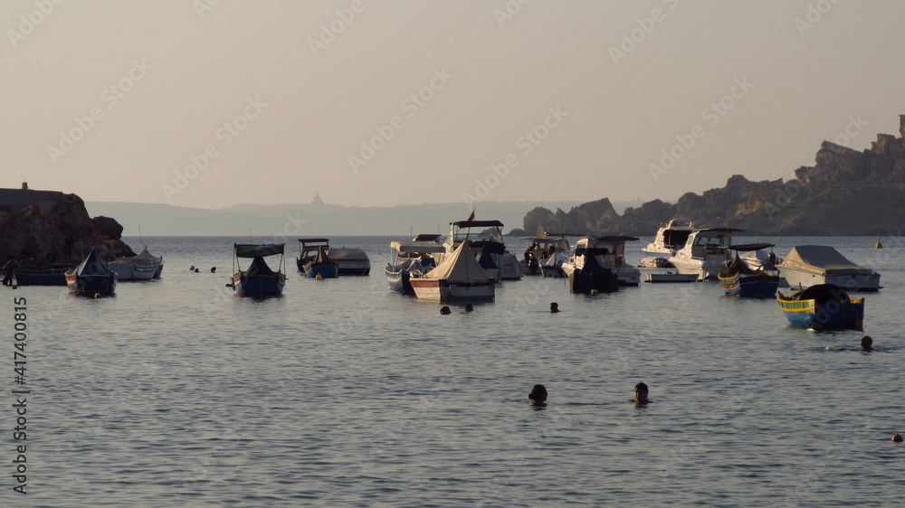 Zatoka z jachtami ze skalistym brzegiem, daleko w tle widać sylwetkę wyspy Gozo, Malta  - obrazy, fototapety, plakaty 