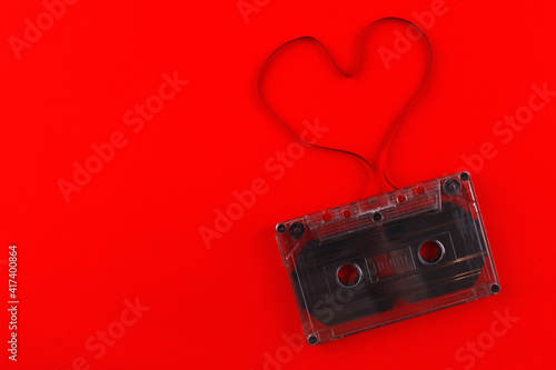 Old black audio cassette on a red background with a heart made of film. Cassette heart