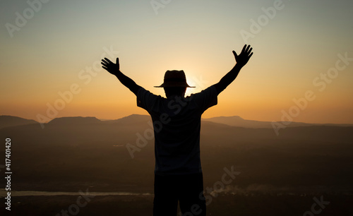 Successful silhouette hiker man standing raised hands on top of mountain, enjoying nature view during sunrise. © Pituk