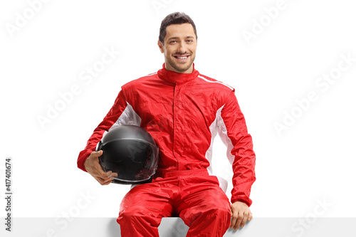 Car racer in a red uniform sitting on a panel holding a helmet © Ljupco Smokovski