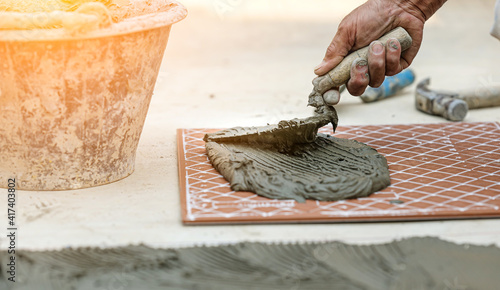 Worker use trowel putting cement on the floor tile in the construction site