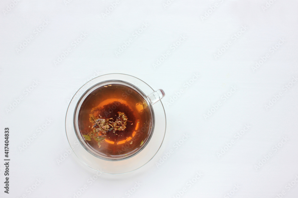 Glass cup of herbal tea with dry oregano flowers on white table background with copy space. Top view. Glass cup of herbal tea with dry oregano flowers on white table background with copy space. Top view.