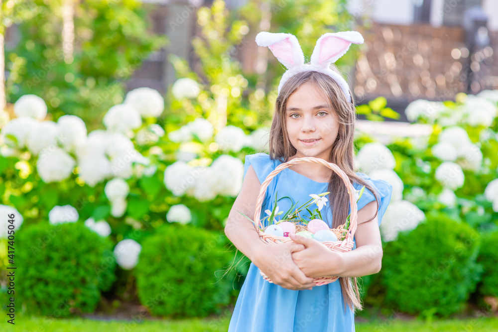 Happy young girl wearing Easter bunny ears holds basket of a Easter eggs. Empty space for text Happy young girl wearing Easter bunny ears holds basket of a Easter eggs. Empty space for text