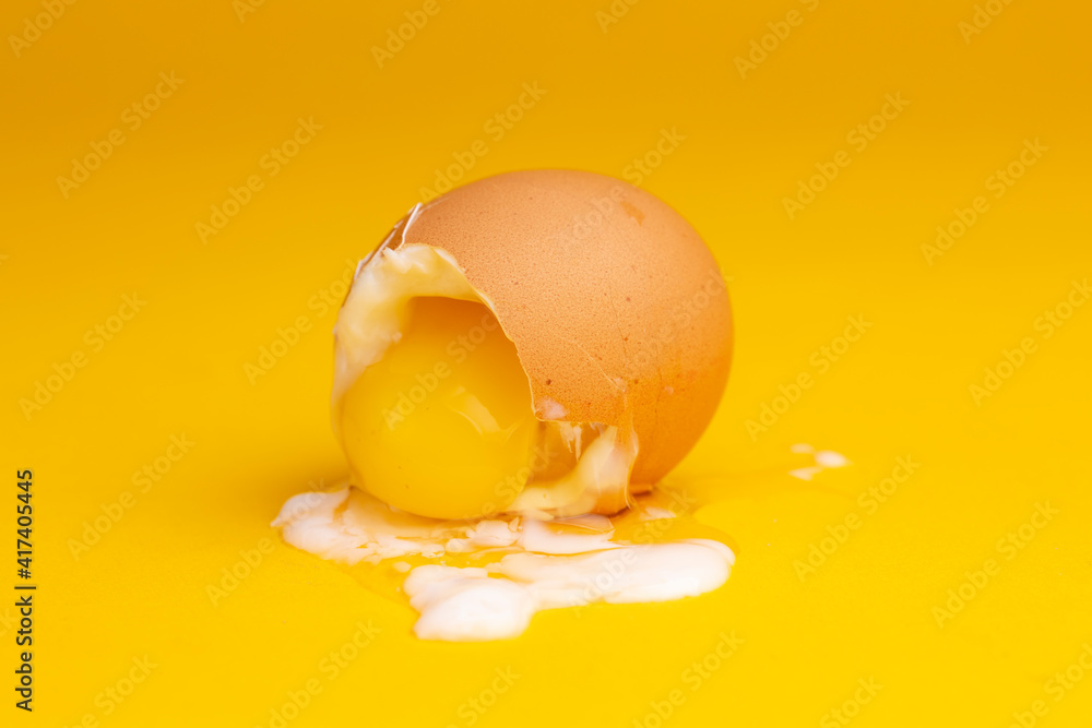 Yolk spilling out broken shell of soft cooked egg with the slimy white wetting the seamless yellow background. Studio food still life against an even colorful backdrop. Yolk spilling out broken shell of soft cooked egg with the slimy white wetting the seamless yellow background. Studio food still life against an even colorful backdrop.