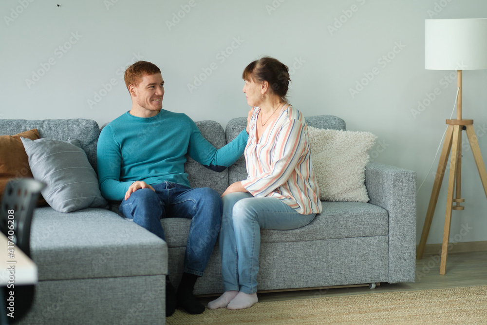 Cheerful elderly woman sitting on the sofa next to his adult son. adult son and mom talk to each other Cheerful elderly woman sitting on the sofa next to his adult son. adult son and mom talk to each other