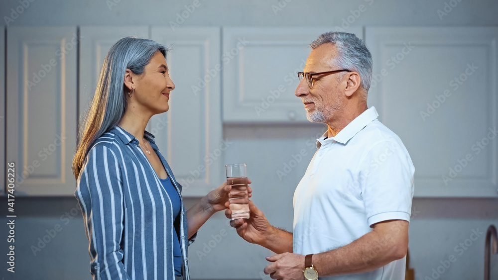 side view of senior man giving glass of water to happy asian wife side view of senior man giving glass of water to happy asian wife