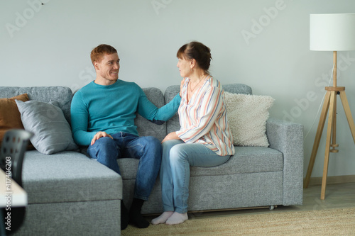 Cheerful elderly woman sitting on the sofa next to his adult son. adult son and mom talk to each other