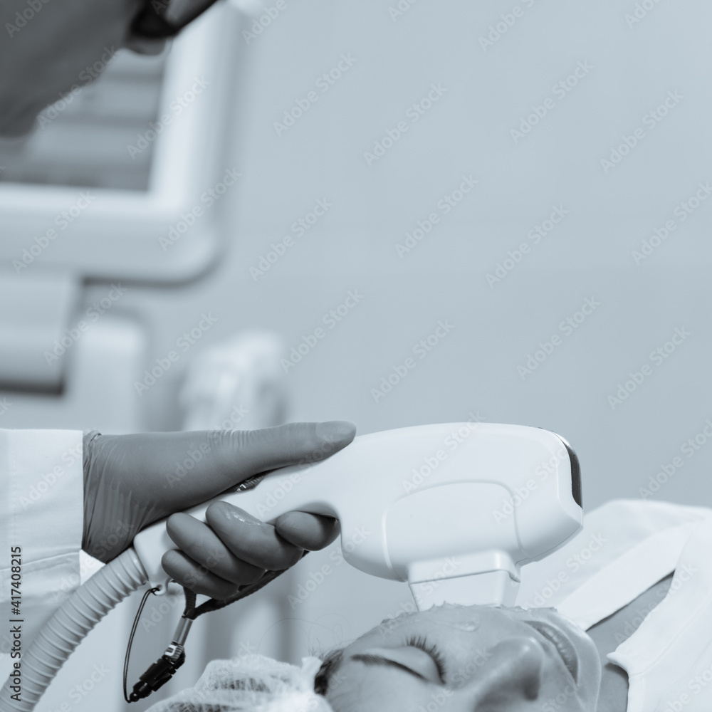 Woman receiving face skin phototherapy procedure in clinic of aesthetic cosmetology. black and white image with blue tint to emphasize the concept of high technology Woman receiving face skin phototherapy procedure in clinic of aesthetic cosmetology. black and white image with blue tint to emphasize the concept of high technology