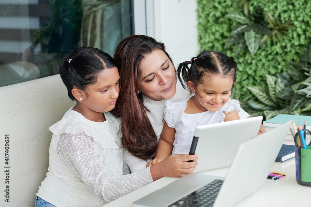 Cheerful mother and two girls sitting at table in backyard and watching animated movie on tablet computer Cheerful mother and two girls sitting at table in backyard and watching animated movie on tablet computer