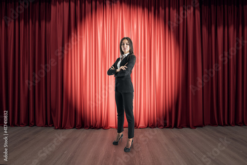 Businesswoman speaker on the stage with wooden floor, in front of red curtains with round spotlight