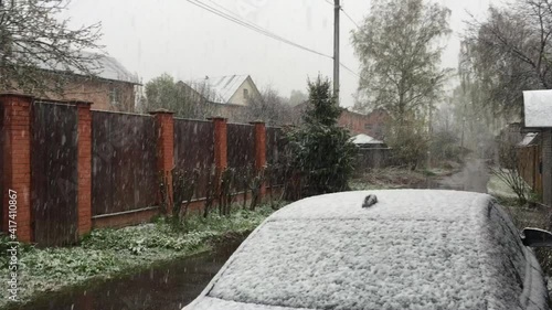 Abnormal spring weather, fluffy snow covers the street with a parked car.