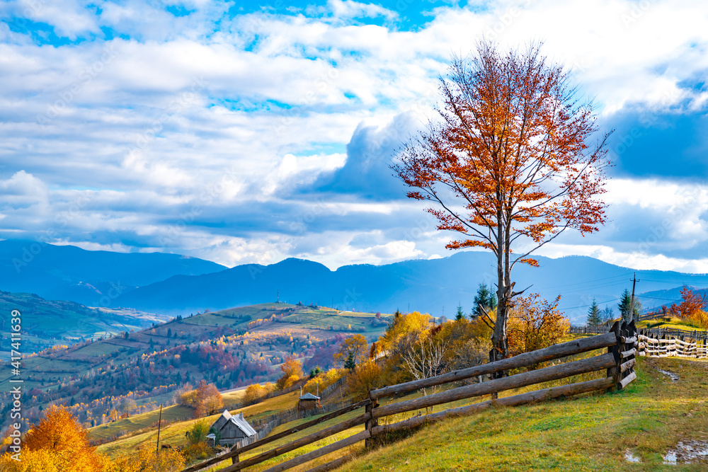 Fototapeta premium Village under the hills sheltered by autumn forests in the light of the bright sun in good weather