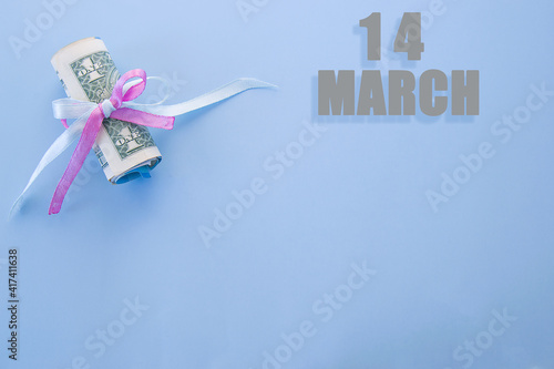 calendar date on blue background with rolled up dollar bills pinned by blue and pink ribbon with copy space. March 14 is the fourteenth day of the month
