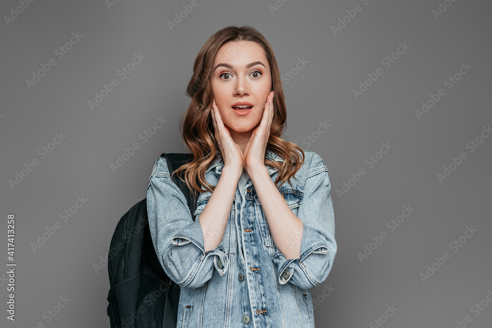 Shocked caucasian student girl holding her face with two hands and looking at the camera isolated on dark gray background in studio. Exams concept Shocked caucasian student girl holding her face with two hands and looking at the camera isolated on dark gray background in studio. Exams concept
