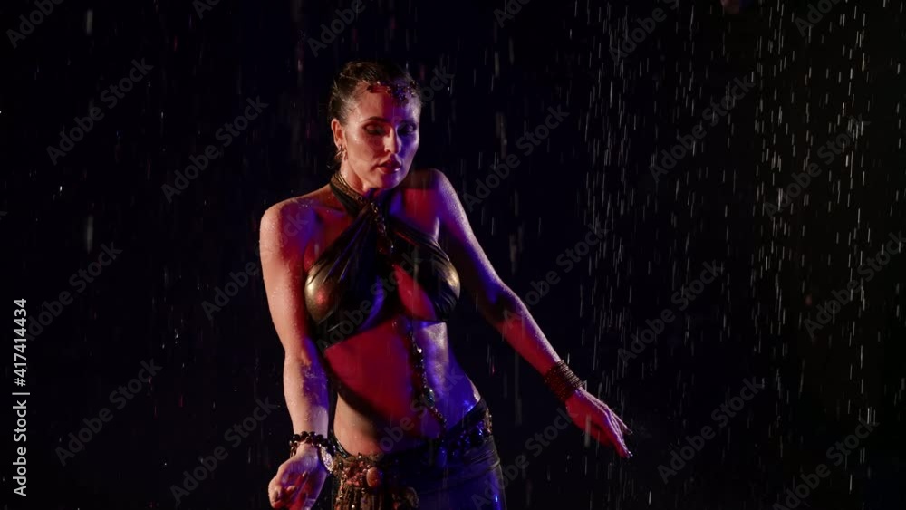 A beautiful woman dances an oriental dance on a black background in the pouring rain in the studio. Makes movements with her hands. A beautiful woman dances an oriental dance on a black background in the pouring rain in the studio. Makes movements with her hands.