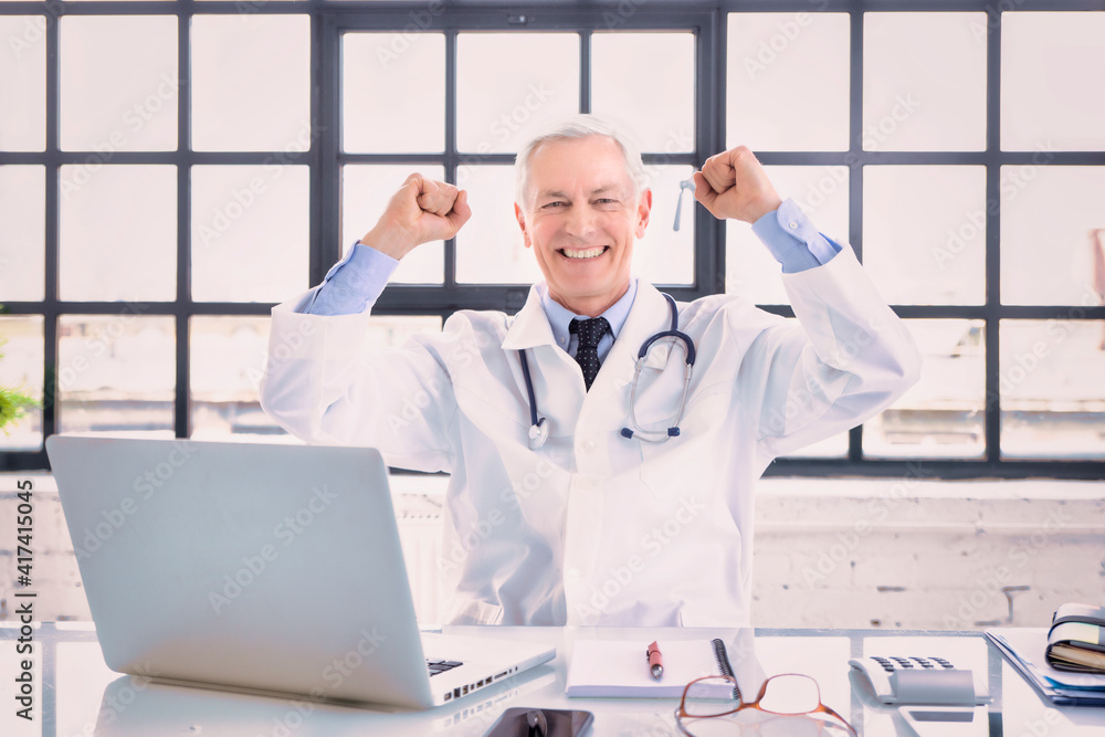 Successful male doctor portrait while sitting behind his laptop at the doctor's office Successful male doctor portrait while sitting behind his laptop at the doctor's office