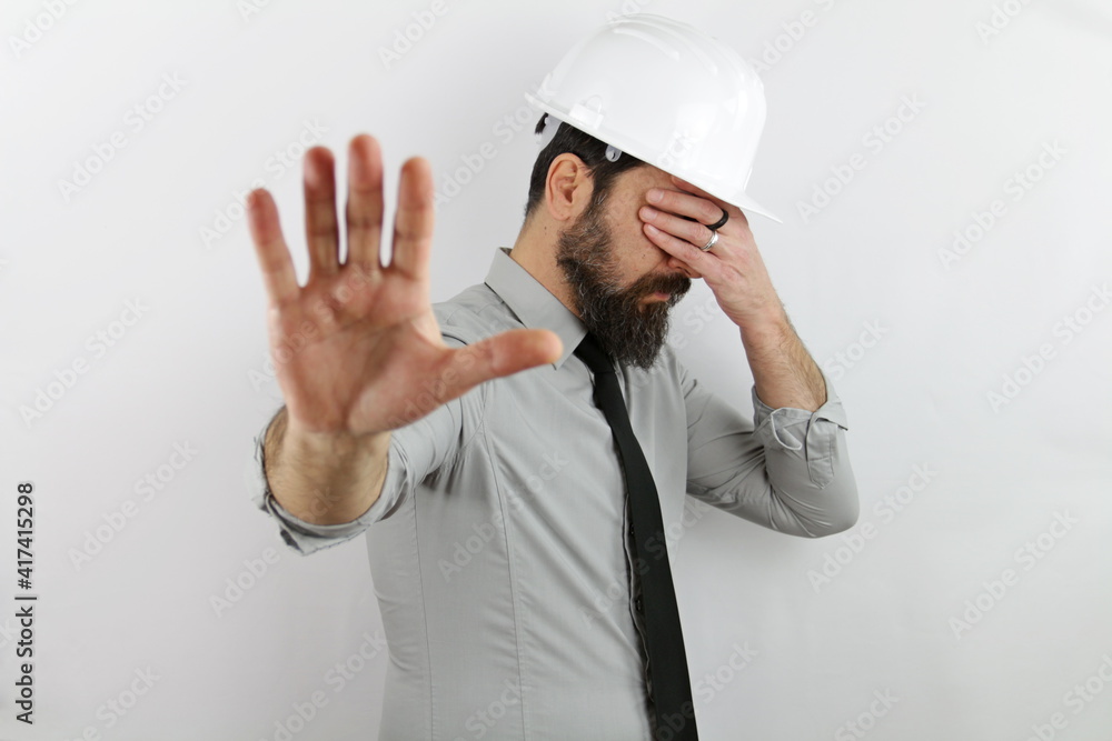 Builder man wearing hardhat and reflecting jacket in shock covering face and eyes with hand with embarrassed expression and doing stop gesture with fear expression. Builder man wearing hardhat and reflecting jacket in shock covering face and eyes with hand with embarrassed expression and doing stop gesture with fear expression.