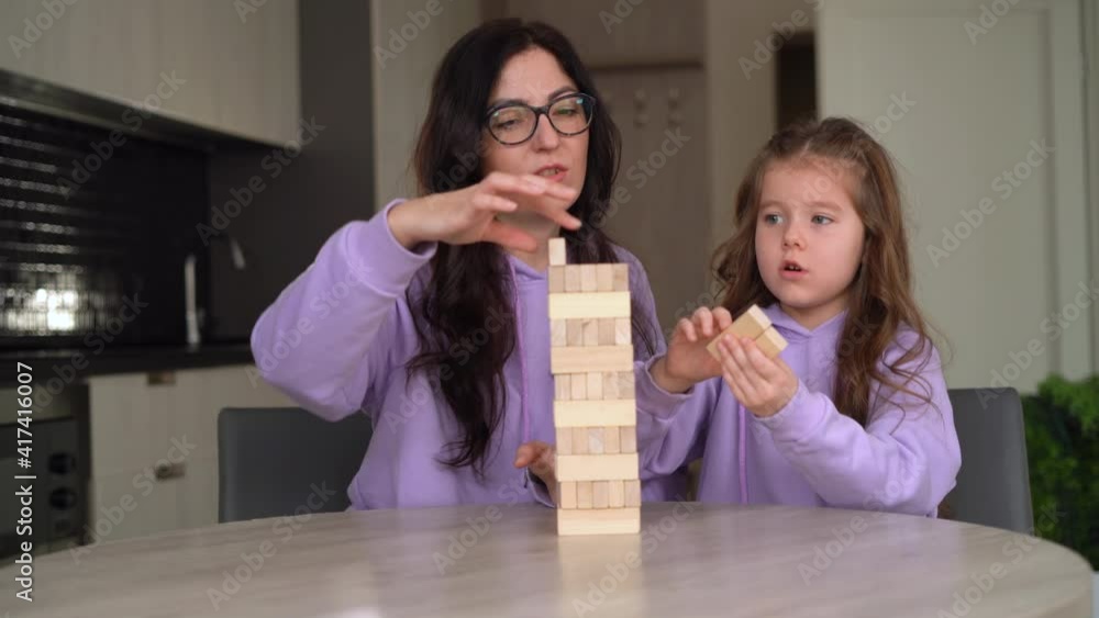 Young brunette mom wearing glasses plays a wooden board game with her little daughter 5 years old. Motherhood and childhood concept. Child development. Young brunette mom wearing glasses plays a wooden board game with her little daughter 5 years old. Motherhood and childhood concept. Child development.