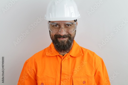 Handsome man with beard wearing worker uniform and hardhat smiling looking at the camera