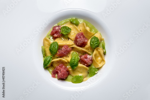 Ravioli del plin with broad beans sauce  Bra sausage and basil leaves  typical stuffed pasta from Langhe  Italy. Top view