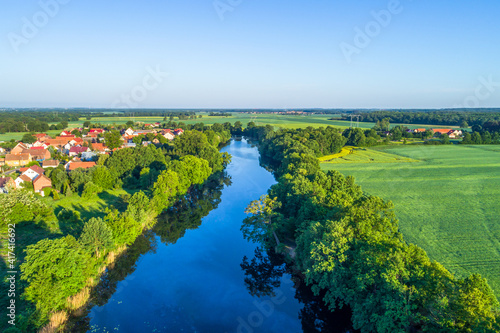 A lake or river with dark blue water and surrounding trees and green fields. Rural areas with buildings.