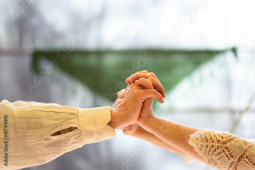 Joined and intertwined hands of a couple dressed in white.