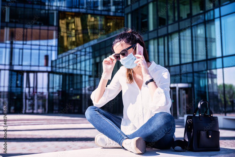 Fototapeta premium Confident woman wearing face mask while sitting on the street and making a call
