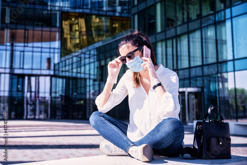 Confident woman wearing face mask while sitting on the street and making a call