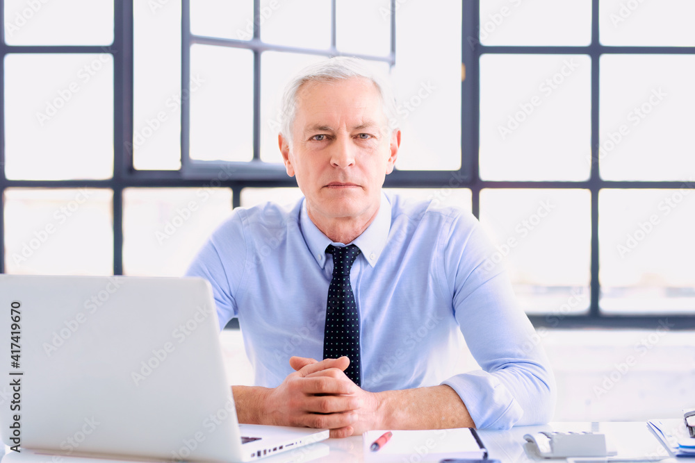 Executive senior businessman working on his laptop while sitting at desk at the office Executive senior businessman working on his laptop while sitting at desk at the office