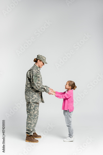 Side view of smiling soldier and daughter holding hands on grey background
