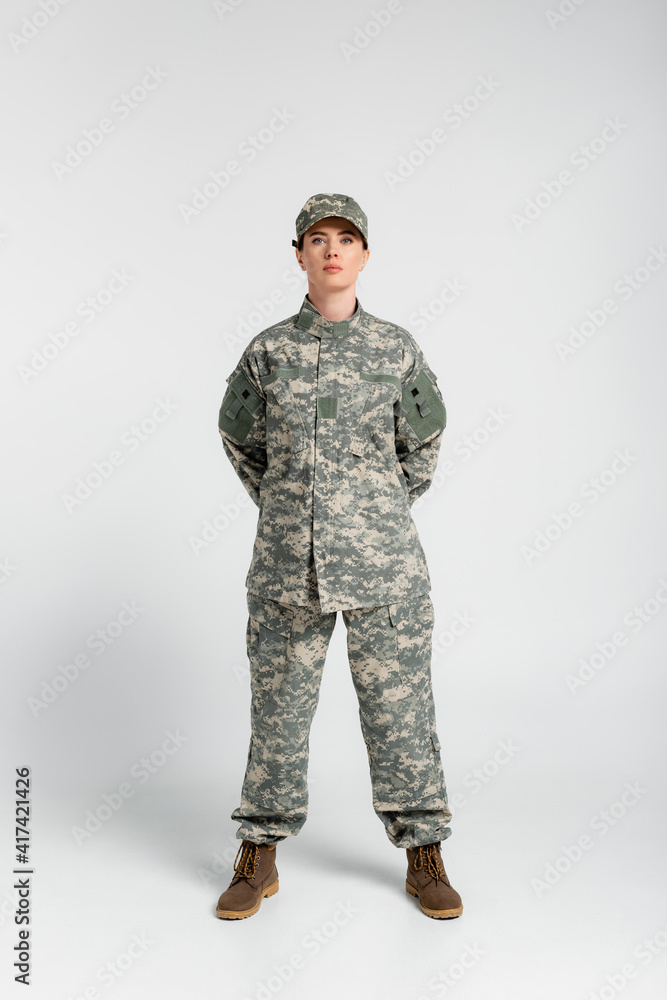 Woman in military uniform and boots looking at camera on grey background Woman in military uniform and boots looking at camera on grey background