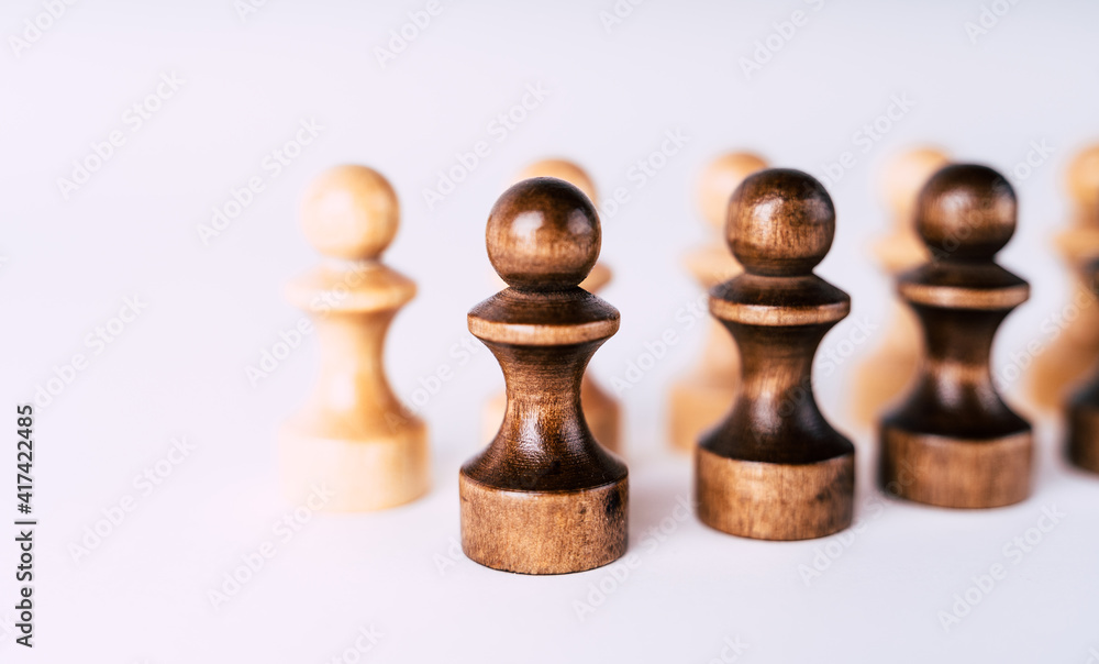 Close up of rows of black and white wooden chess pieces on white background. Selective focus on black pawns. Close up of rows of black and white wooden chess pieces on white background. Selective focus on black pawns.
