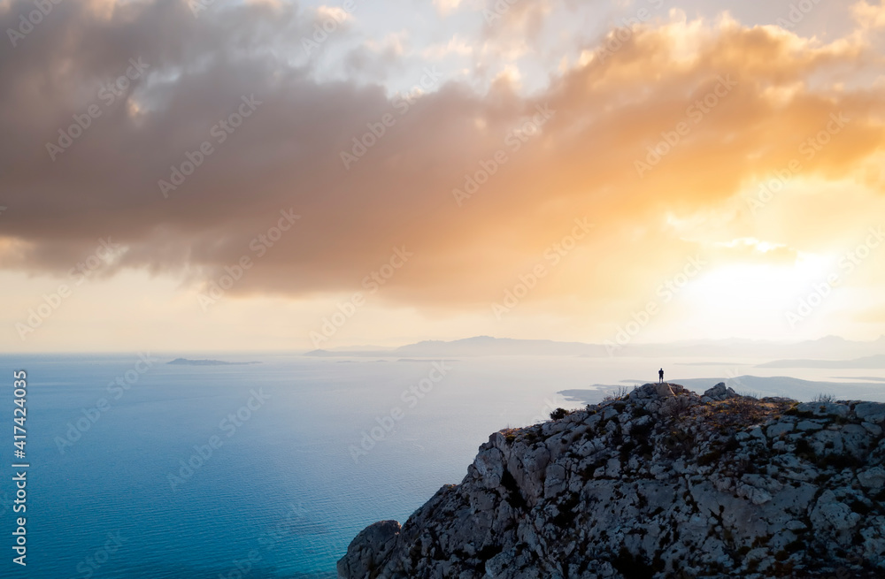 View from above, stunning aerial view of a person enjoying a beautiful sunset from the summit of a mountain, Golfo Aranci, Sardinia, Italy.