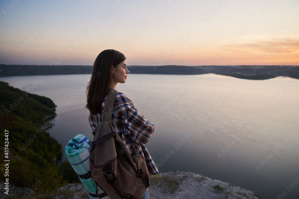 Pleasant woman standing on hill and looking at sunset