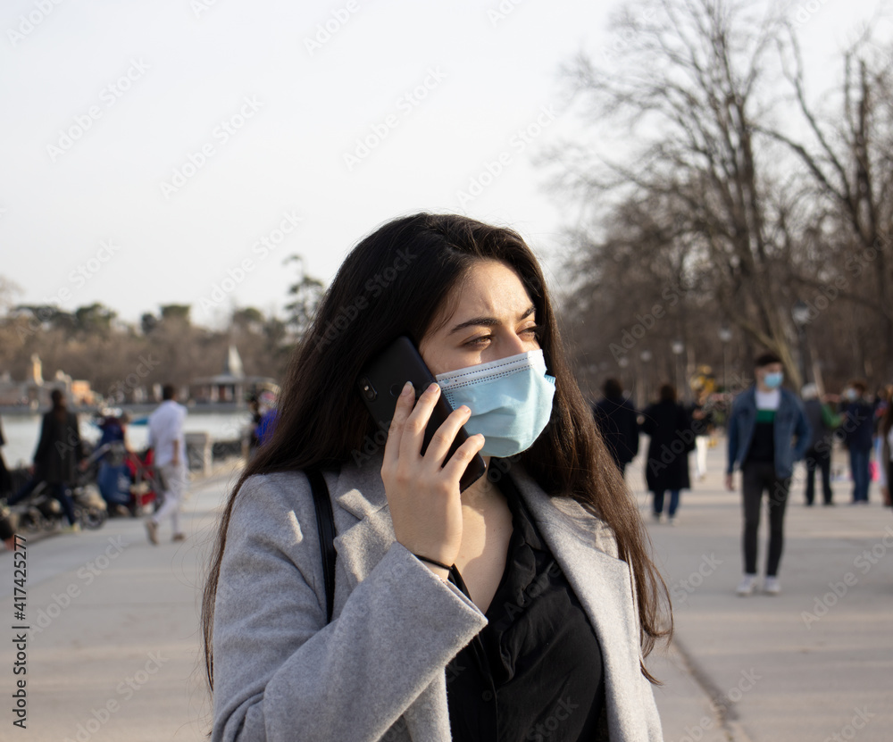 Woman with face mask talking with her mobile in a park.
