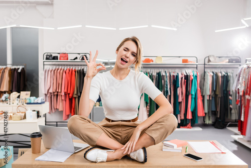 Blonde seller winking and showing ok gesture on table in showroom