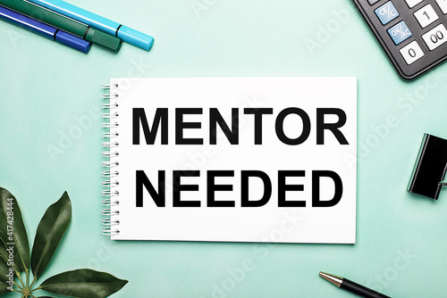 MENTOR NEEDED is written on a white sheet on a blue background near the stationery and the Scheffler sheet. Call to action. Motivational concept photo