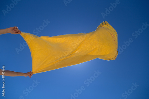 Female hands holding yellow towel against the blue sky.
