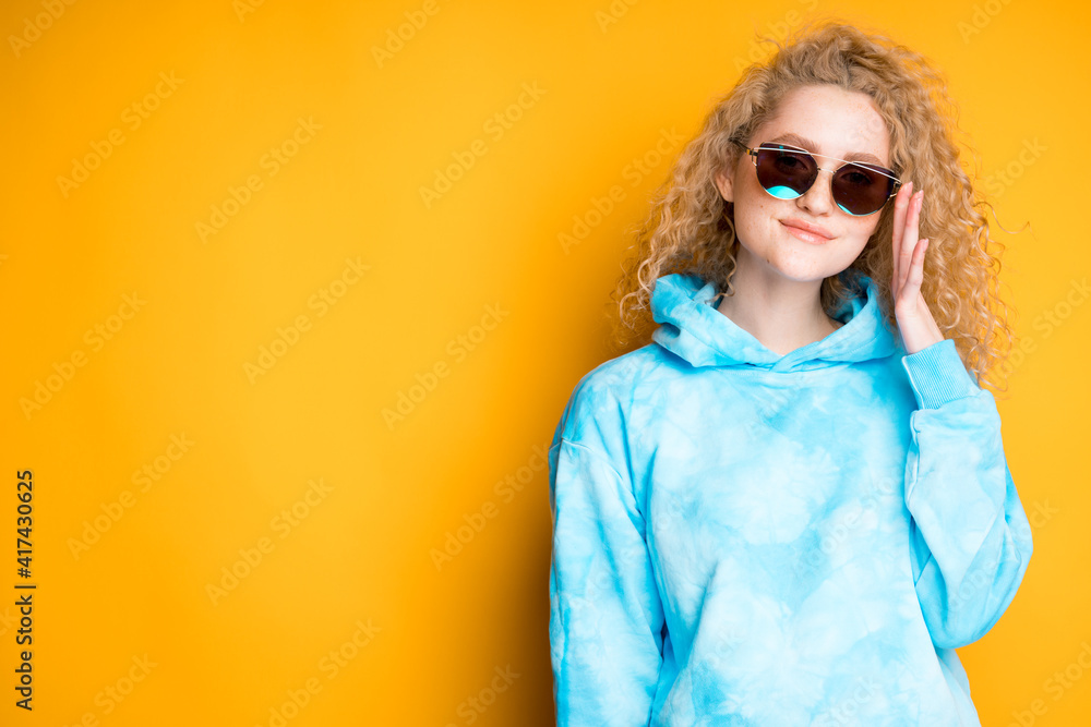 Fototapeta premium Charming woman with curly hair stands in glasses on an orange background. Summer concept
