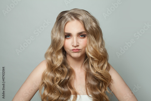 Young funny woman with long perfect hair grimacing on white background
