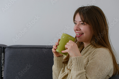 Mujer latina sonriendo mientras toma una taza de café por la mañana mientras descansa en la sala de su casa.