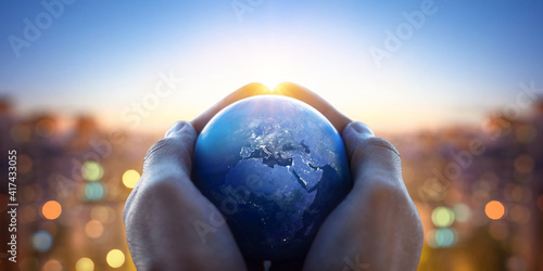 Planet Earth in the hands of a man against the background of the lights of the evening city. Concept and symbol on the theme of ecology, earth conservation, news and religion.