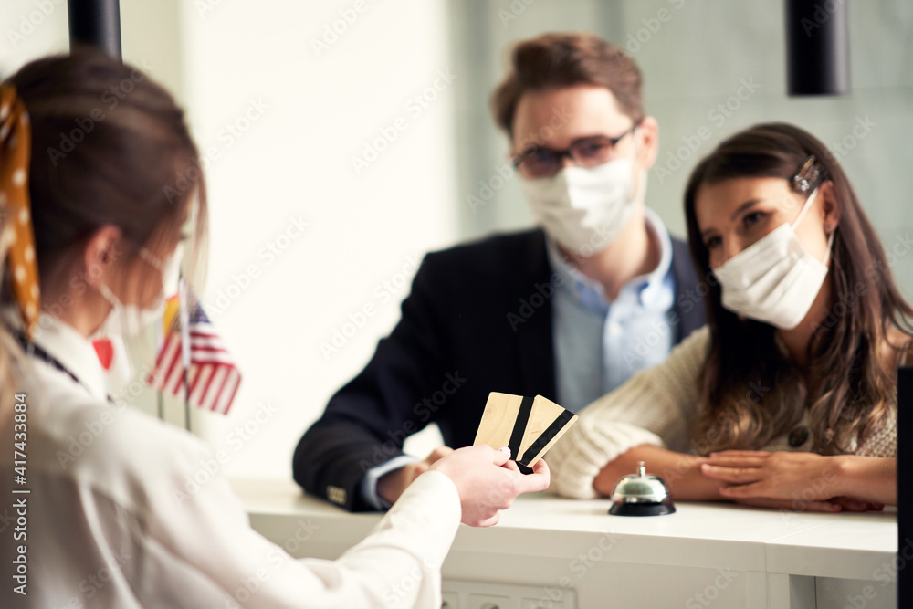 Fototapeta premium Adult couple wearing masks checking-in a hotel