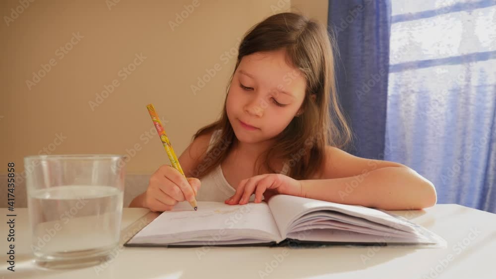 Cute child girl drinks water from glass while drawing with pencil in her sketchbook Cute child girl drinks water from glass while drawing with pencil in her sketchbook