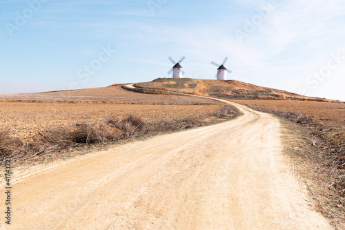 Φωτογραφία two windmills in the countryside with dirt road and straw blue sky, donquijote f