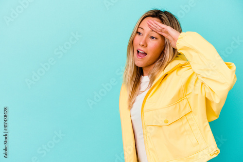 Young mixed race woman isolated on blue background looking far away keeping hand on forehead.
