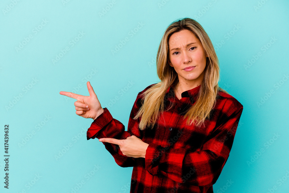 Young mixed race woman isolated on blue background shocked pointing with index fingers to a copy space. Young mixed race woman isolated on blue background shocked pointing with index fingers to a copy space.